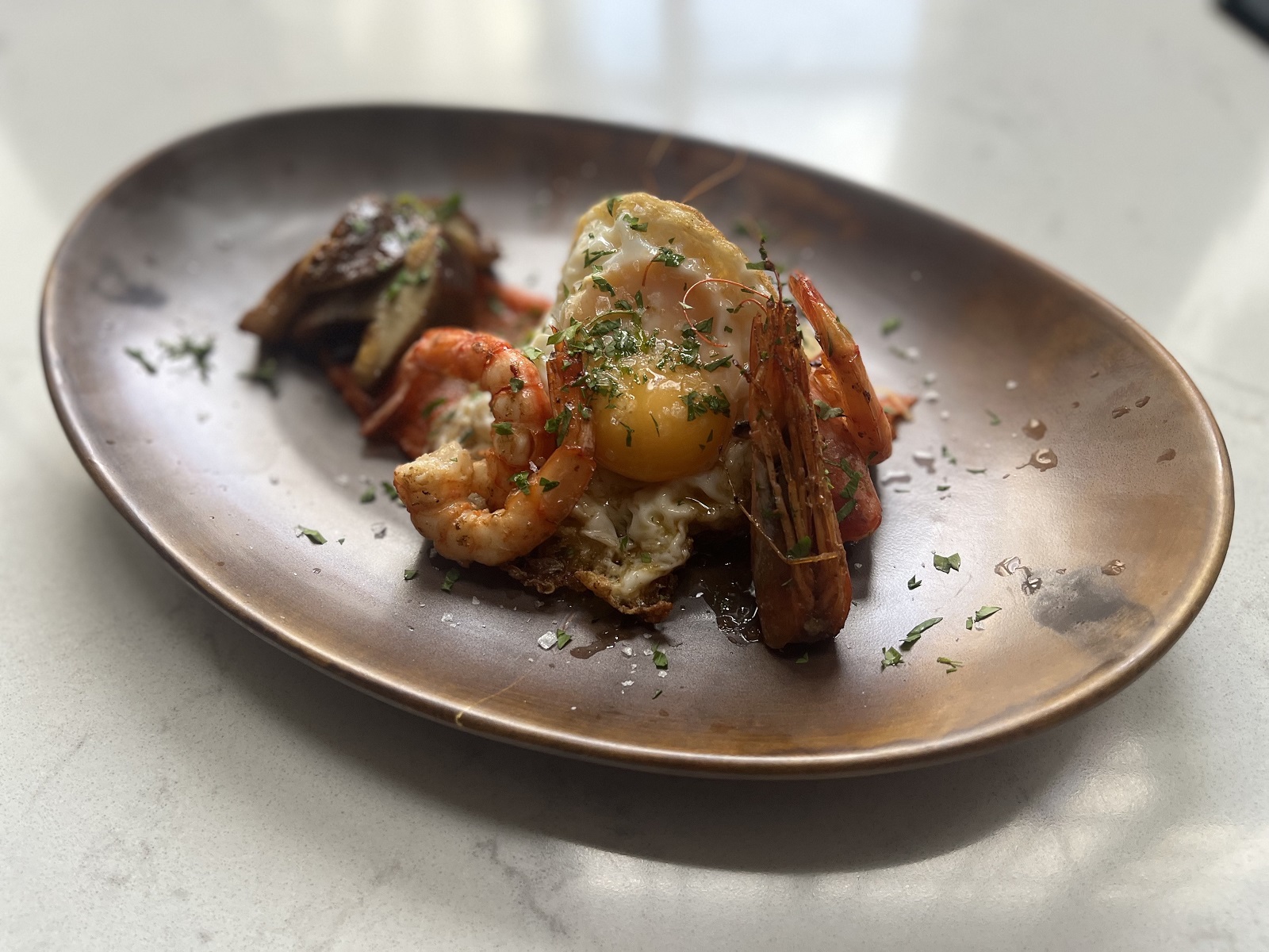 Huevo frito con camarones cristal, hongos, patata frita encebollada, salsa de tomate, alcaravea y guindilla